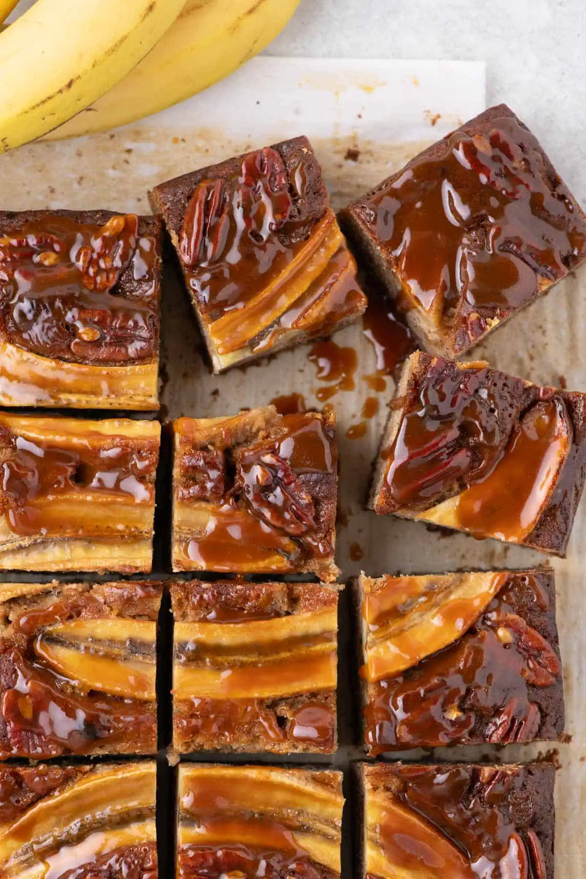 Freshly baked dessert cooling in a parchment-lined pan, topped with sliced bananas and toasted pecans.