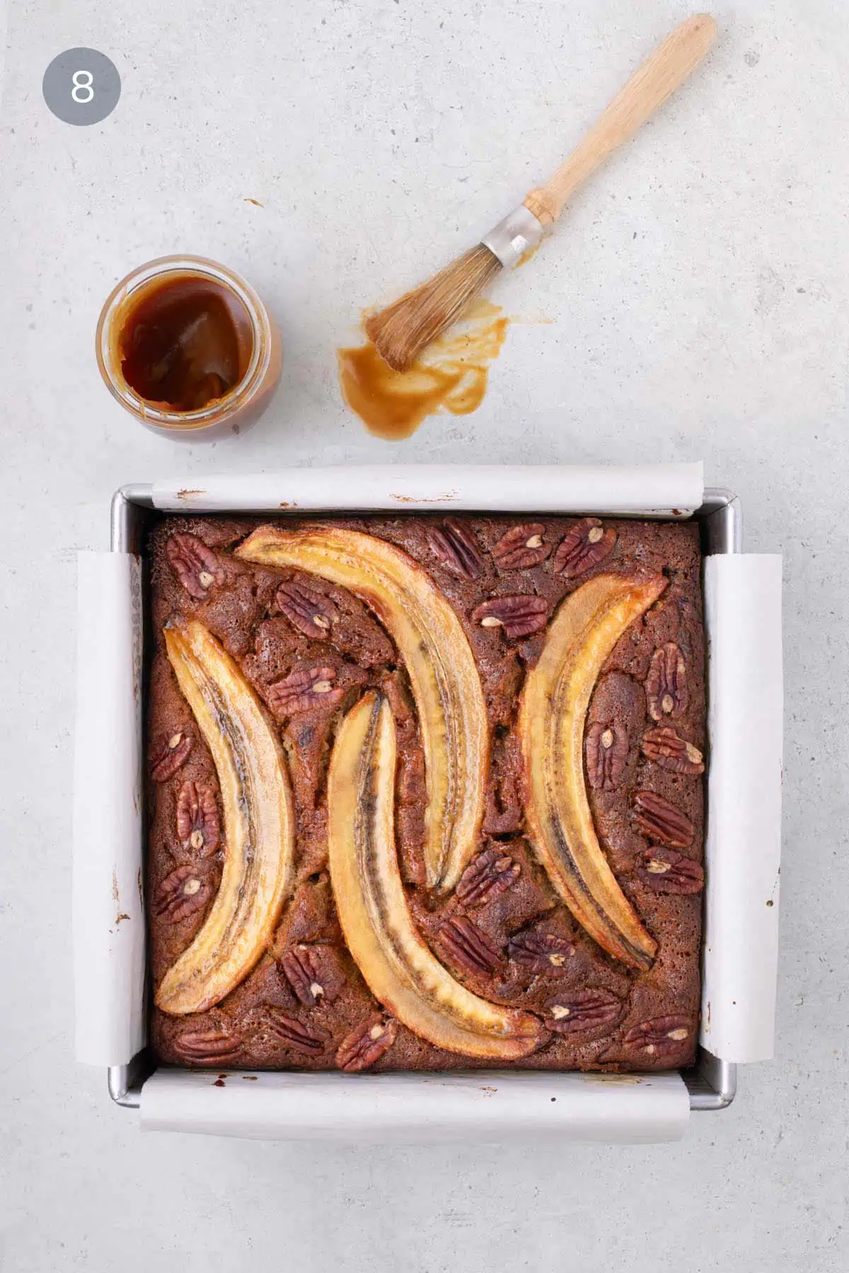 Baked banana bread bars topped with pecans and banana slices, brushed with caramel glaze.