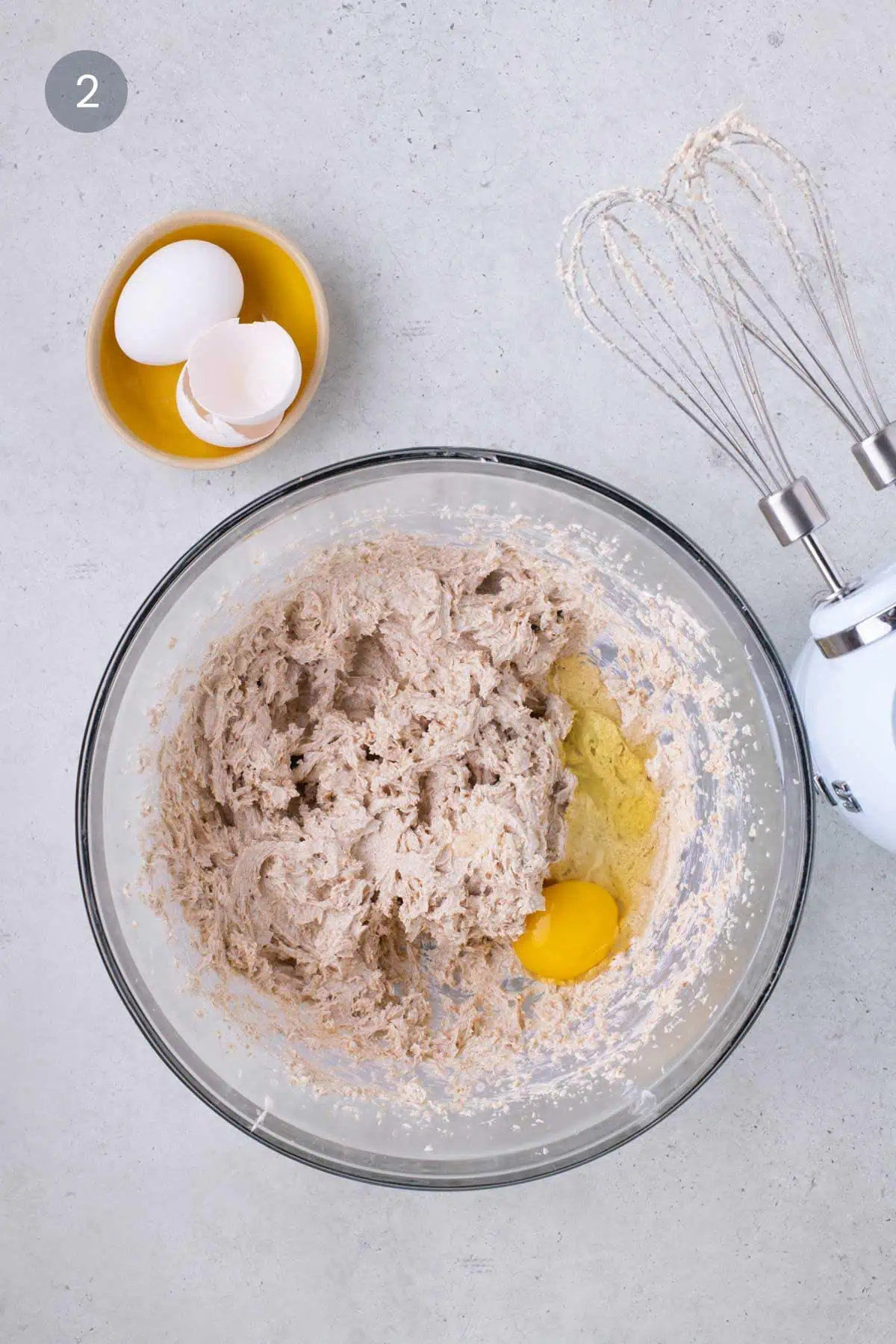 Creamed butter and brown sugar mixture with egg being added in a mixing bowl with a hand mixer.