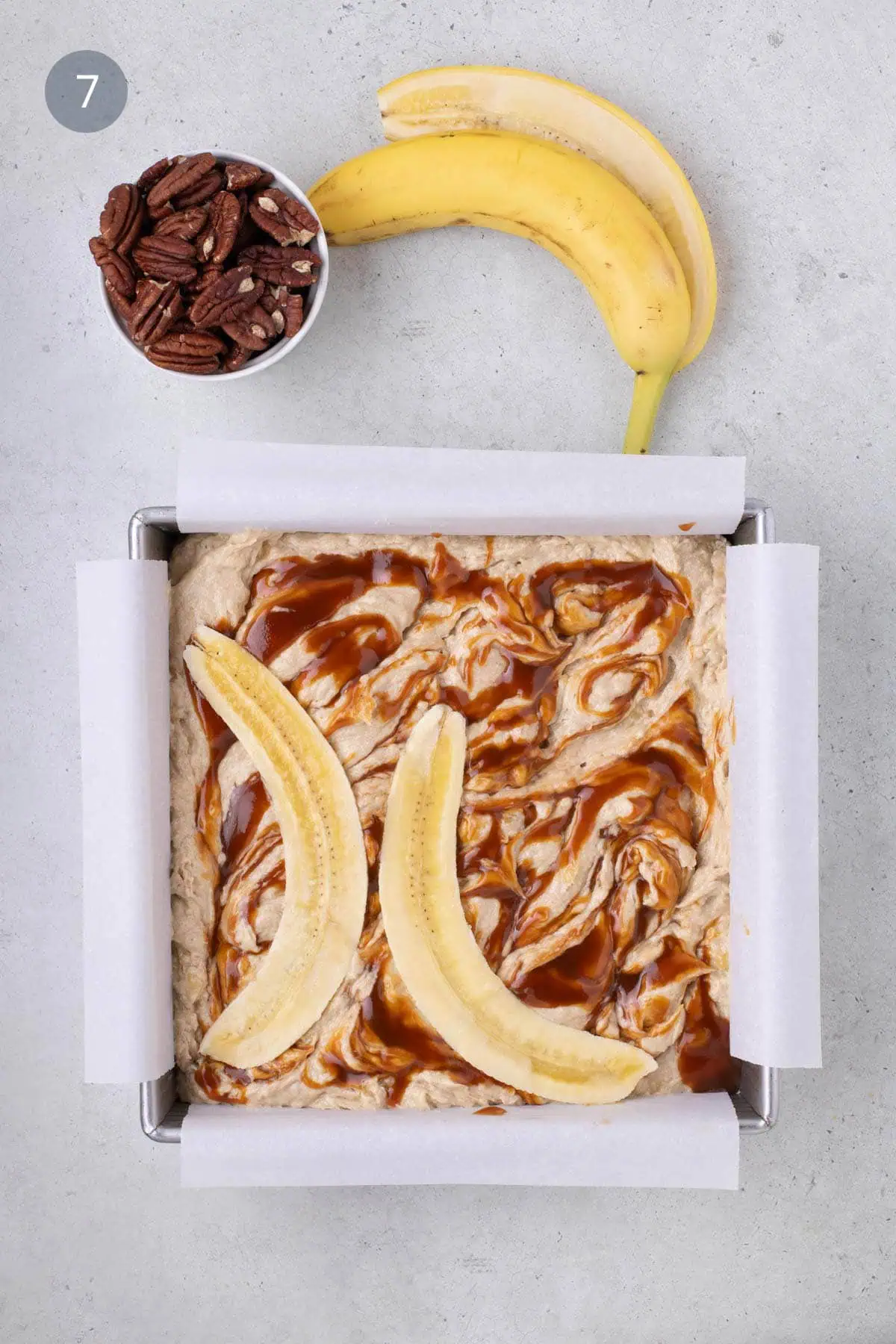 Sliced banana and whole pecans arranged on top of caramel-swirled banana bread batter.
