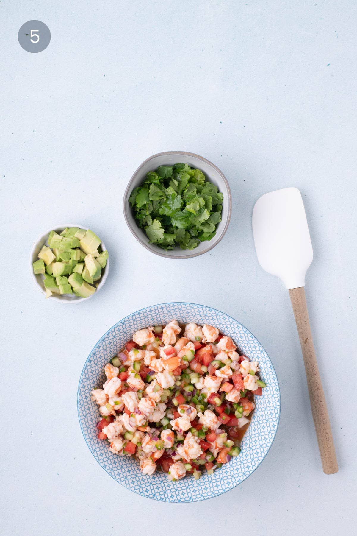 Partially mixed shrimp ceviche in a bowl with chopped avocado and fresh cilantro on the side, ready to be added