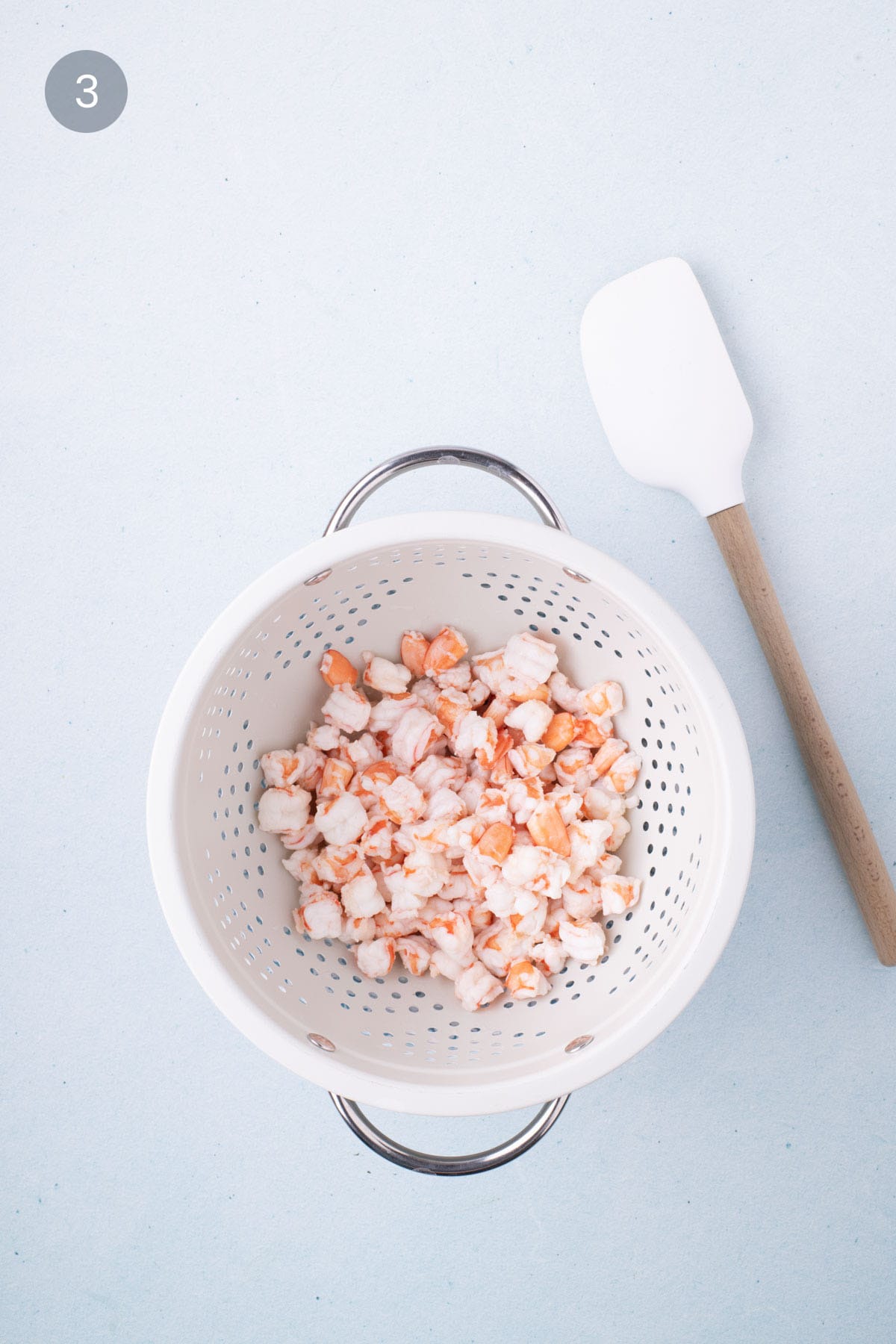 Chopped shrimp in a white colander with a spatula on the side, ready to be used for Mexican shrimp ceviche