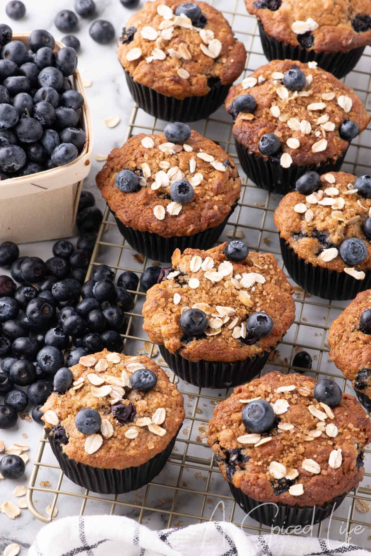 Freshly baked banana and blueberry oat muffins topped with oats and demerara sugar, cooling on a wire rack.