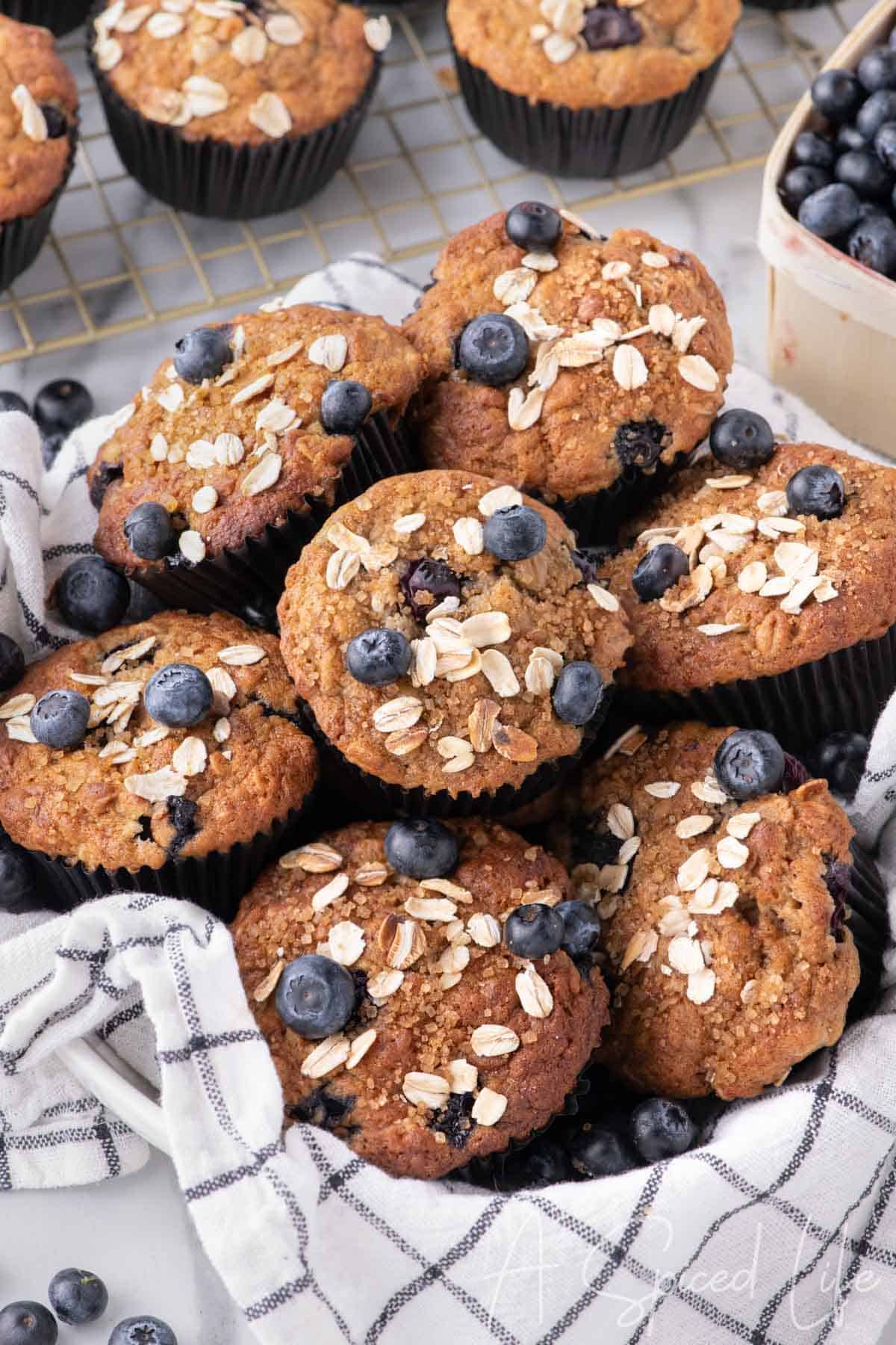 A cozy basket filled with banana blueberry oat muffins, wrapped in a checkered kitchen towel.