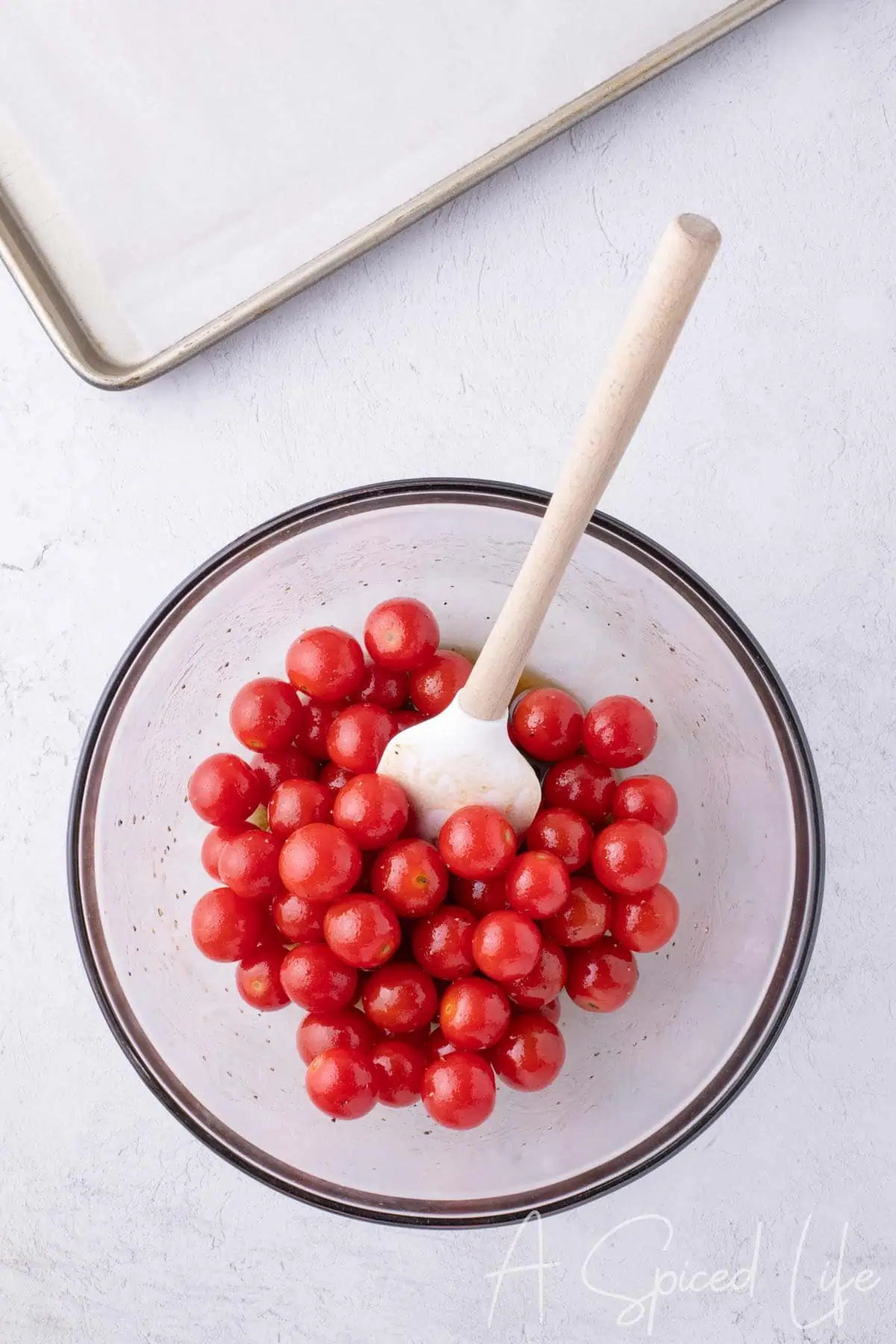 Cherry tomatoes being stirred with a white spatula in a large glass bowl.