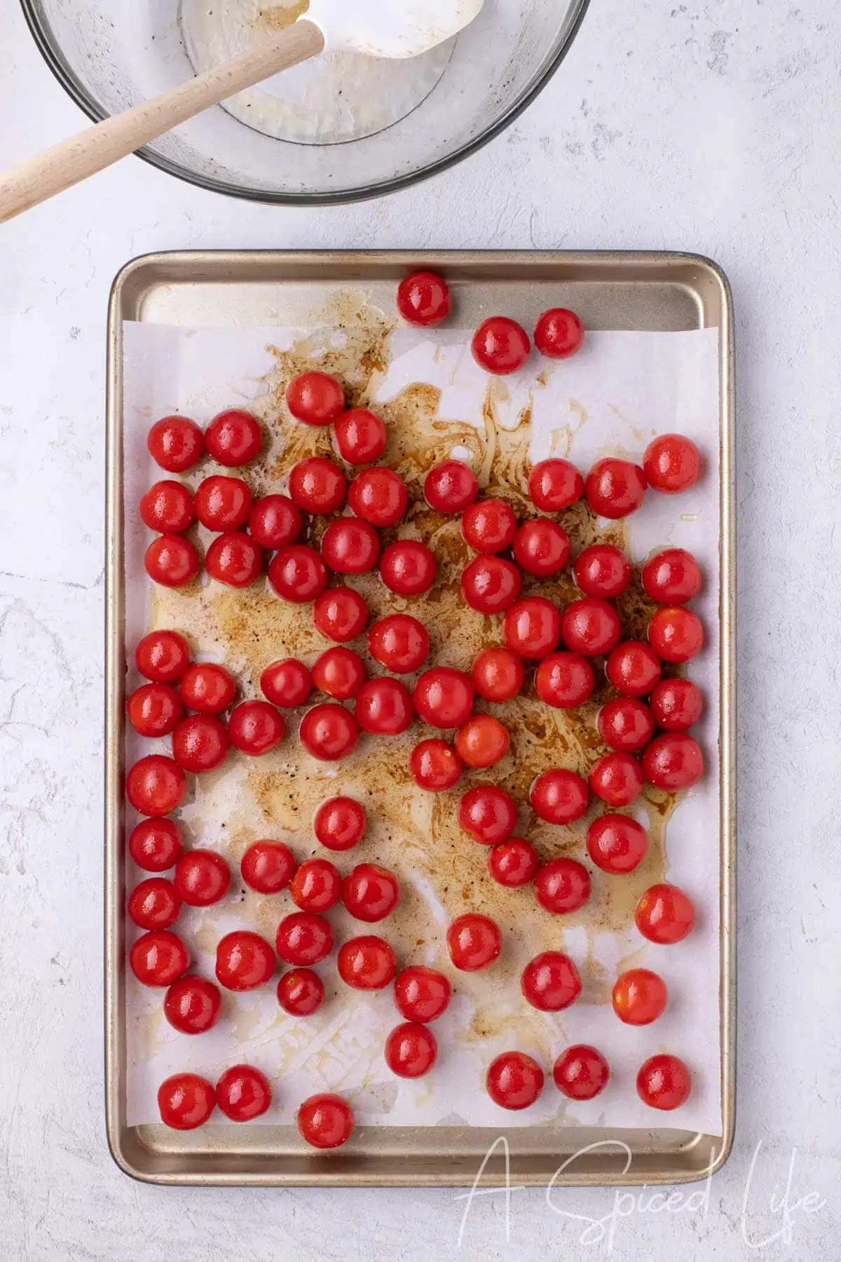 Cherry tomatoes spread in a single layer on a parchment-lined sheet pan.