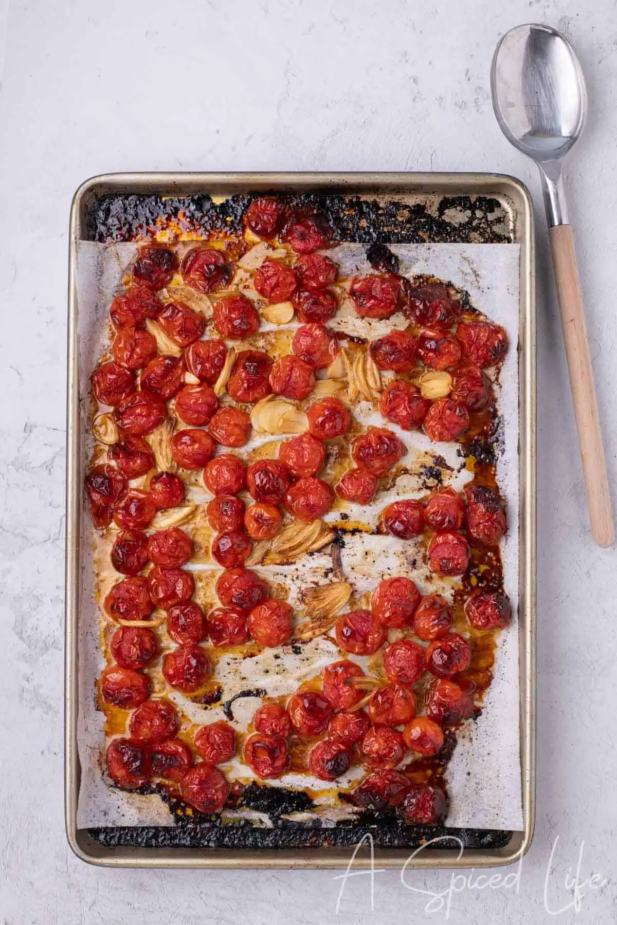 Fully roasted cherry tomatoes and garlic on a parchment-lined sheet pan with charred edges.