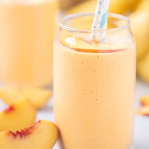 Tropical banana peach smoothie with papaya served in a clear glass with a straw.