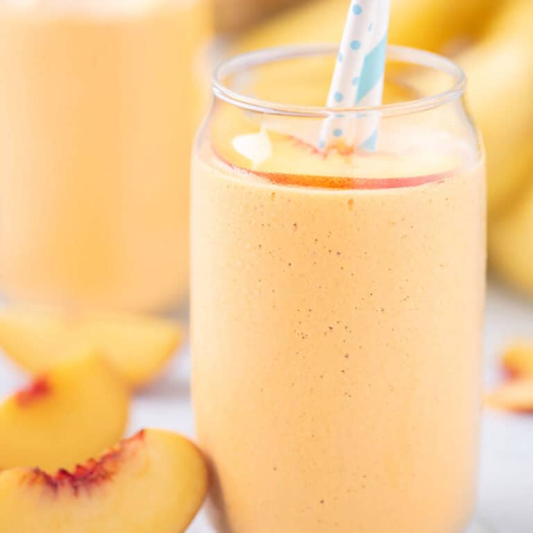 Tropical banana peach smoothie with papaya served in a clear glass with a straw.