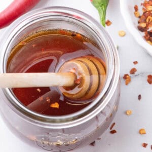 Jar of homemade hot honey with wooden dipper and red chili flakes.