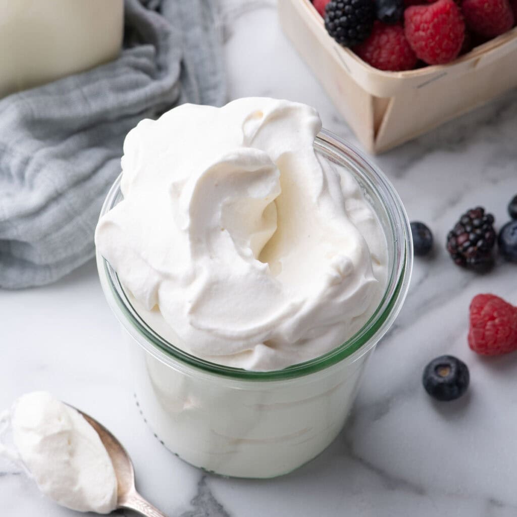 Bowl of Chantilly cream topped with fresh raspberries and blueberries