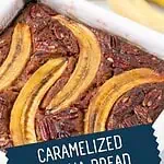 Close-up of caramelized banana bread loaf in a baking pan, topped with banana halves and pecans.