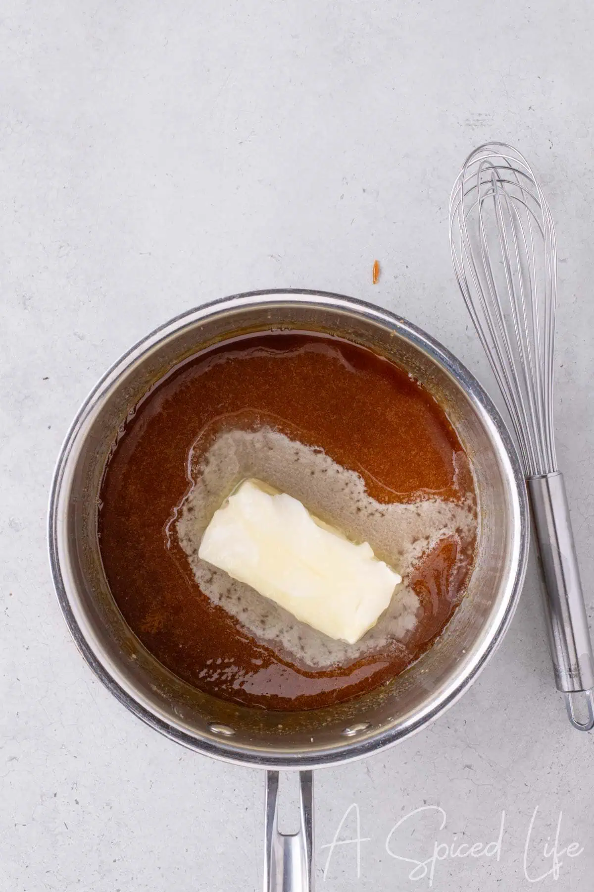 Melted amber colored sugar with a stick of butter added to the saucepan for caramel sauce.