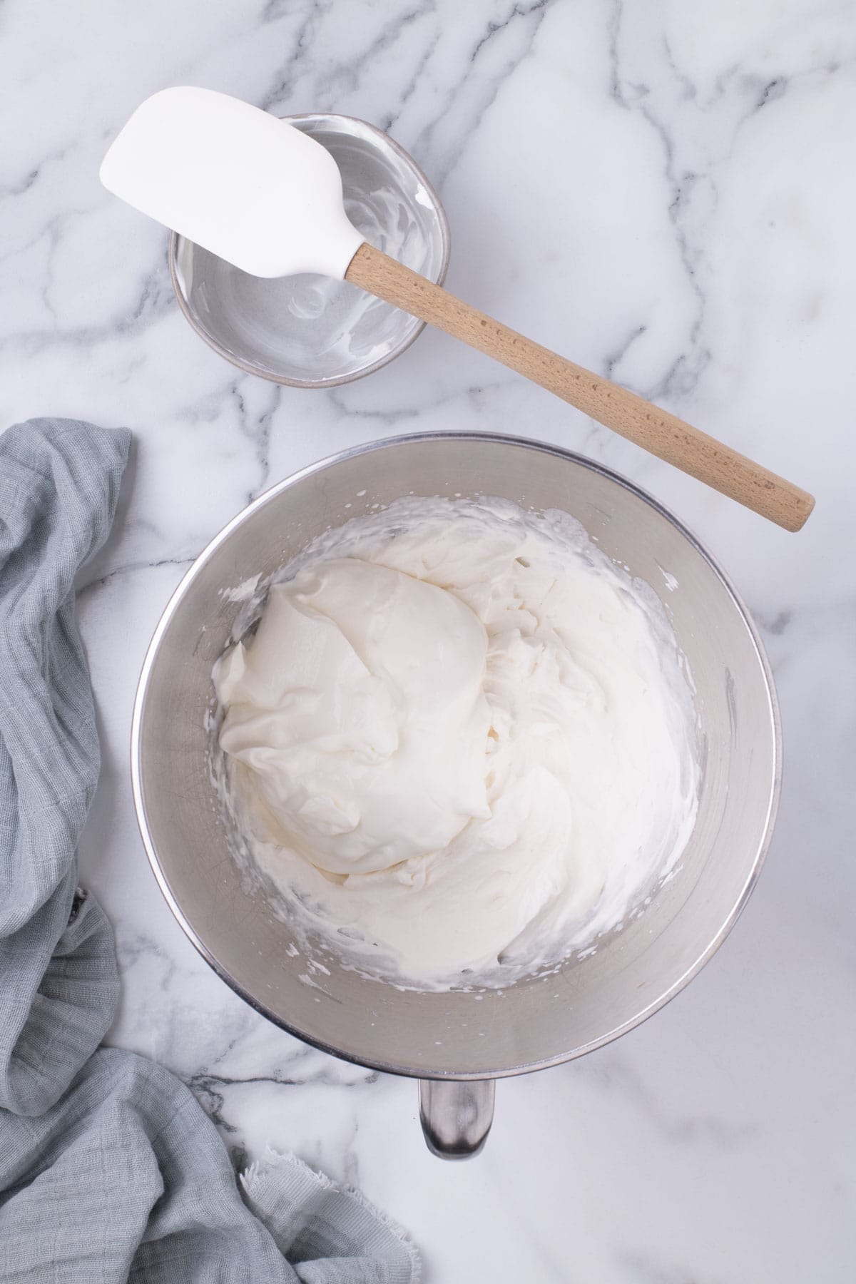 Sour cream being folded into whipped cream in a mixing bowl.