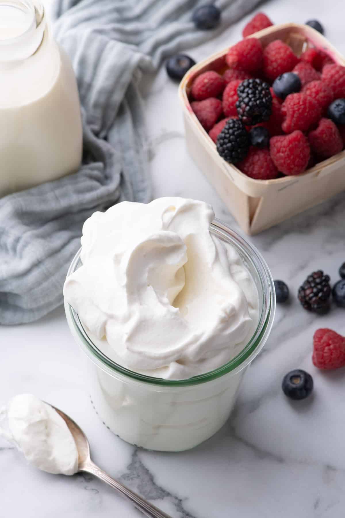 Chantilly cream in a glass jar topped with fresh berries including raspberries and blueberries.