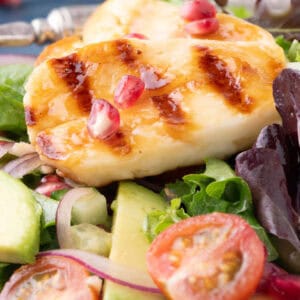 Overhead shot of hot honey halloumi salad with pomegranate, avocado, and grilled cheese slices in a white bowl.