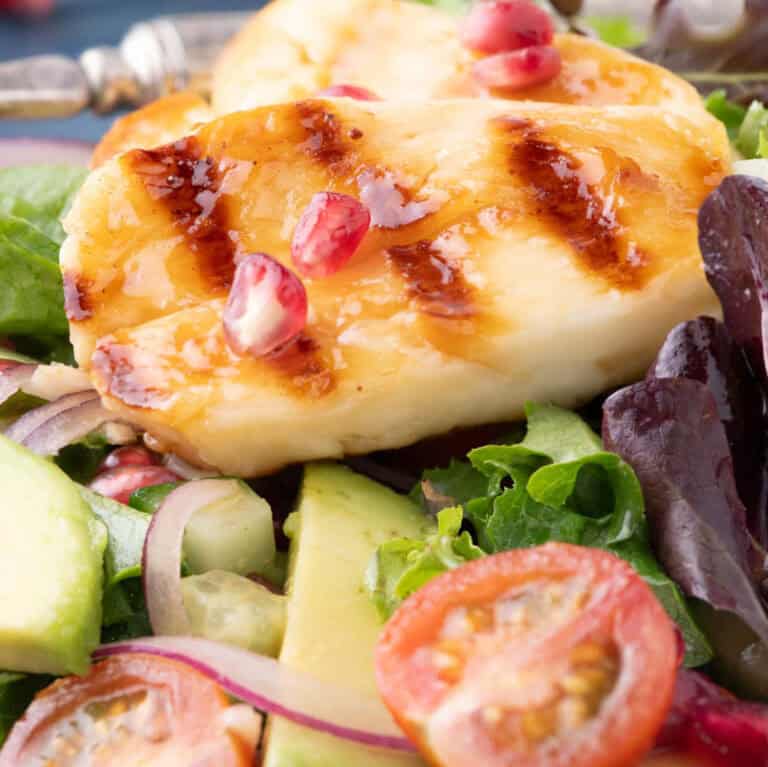 Overhead shot of hot honey halloumi salad with pomegranate, avocado, and grilled cheese slices in a white bowl.