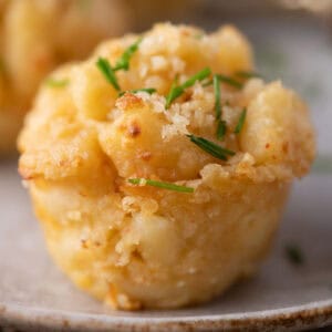 Golden baked mac and cheese bite topped with breadcrumbs and fresh chives on a plate.