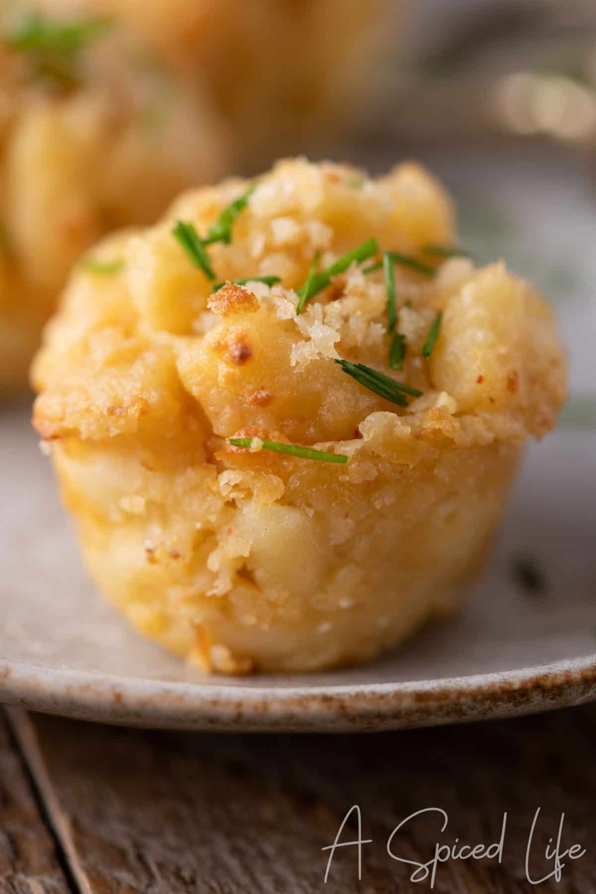 Single golden mac and cheese bite garnished with chives on a plate, styled as an elegant hors d’oeuvre.
