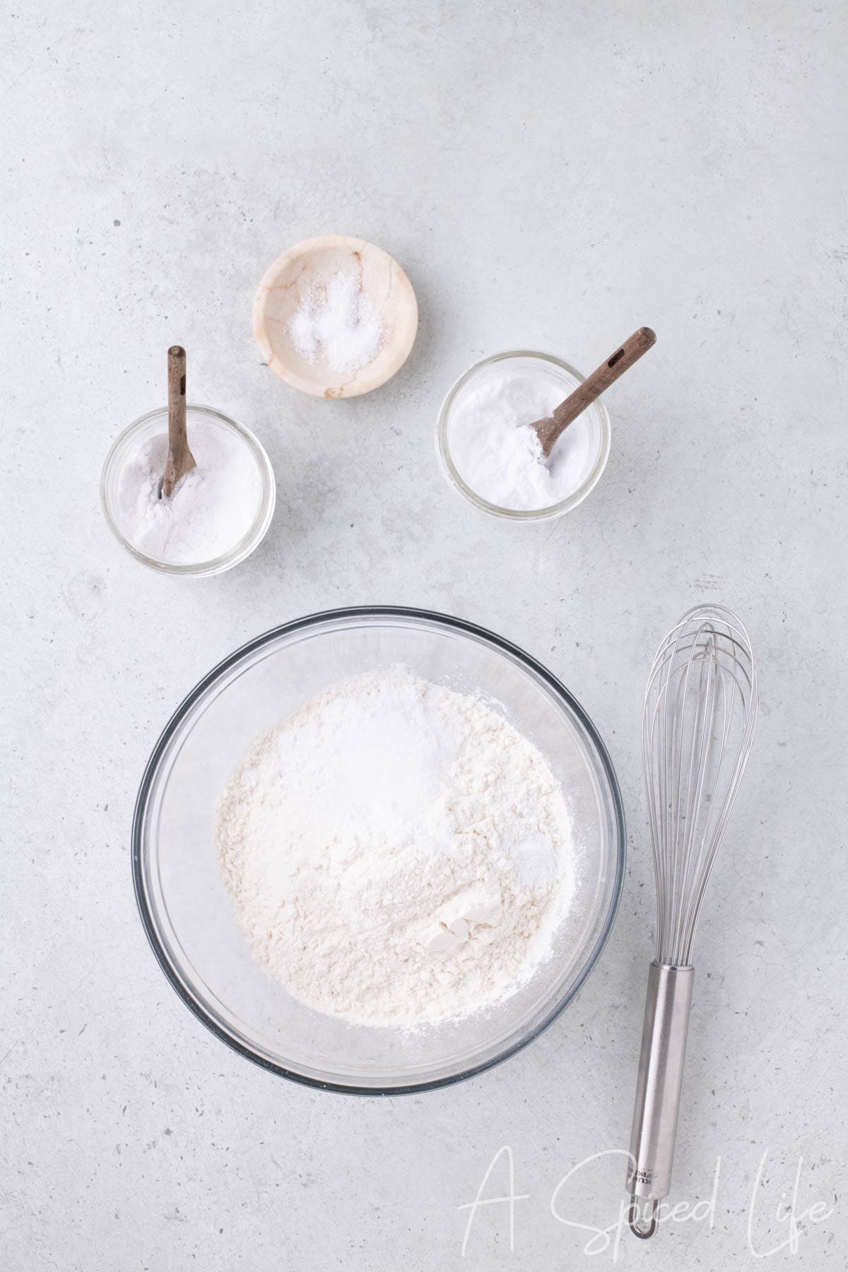 Mixing flour, baking powder, baking soda, and salt in a glass bowl with whisk