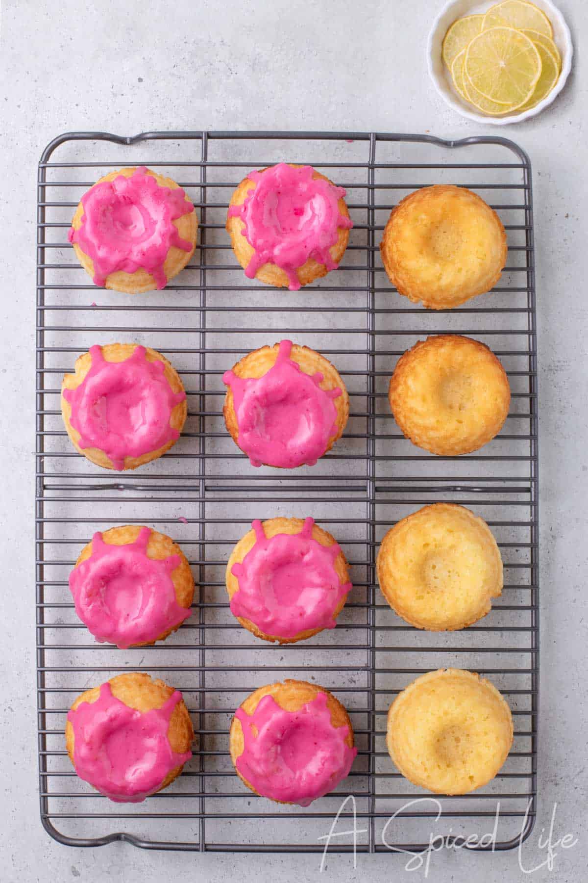 Mini lemon bundt cakes cooling on wire rack, some drizzled with blackberry glaze