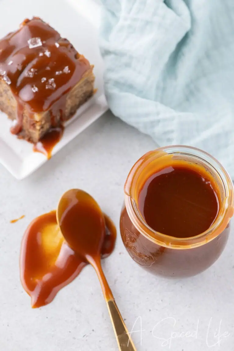 Overhead view of a jar of salted caramel sauce with a spoon and a slice of banana cake topped with caramel and sea salt flakes.