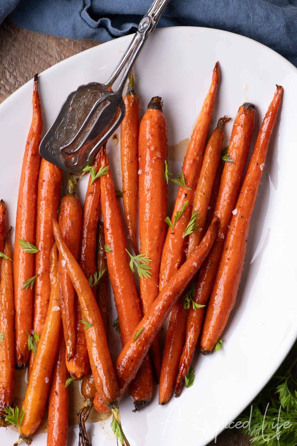 Maple Glazed Carrots served on a white platter with fresh carrot fronds and a buttery maple syrup glaze.