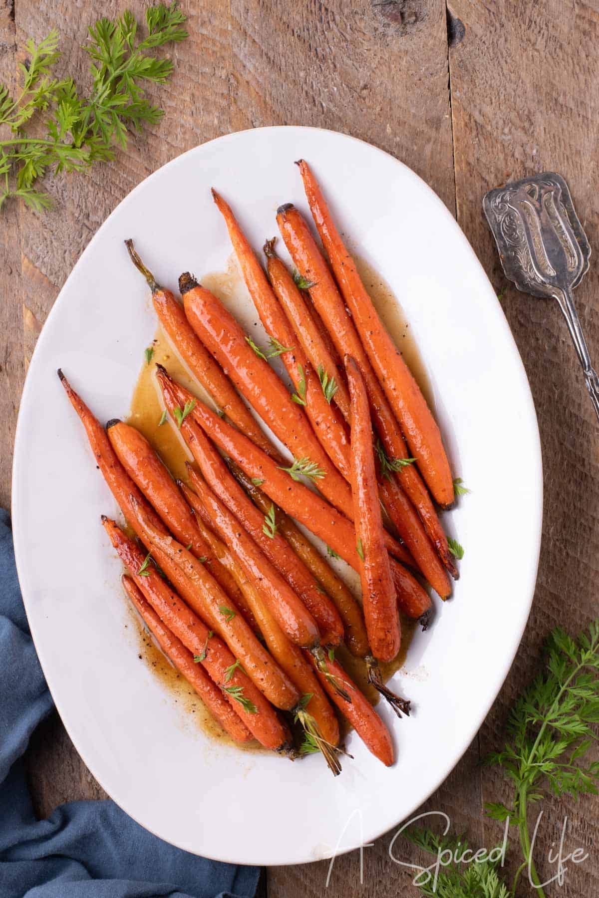 Overhead view of Maple Glazed Carrots served on a white platter with fresh carrot fronds and glossy maple glaze.