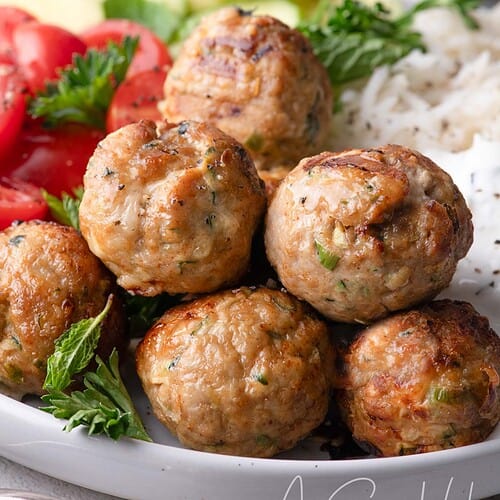 Close up of golden brown turkey feta meatballs with fresh herbs and yogurt sauce