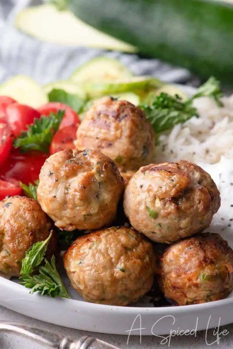 Close up of golden brown turkey feta meatballs with fresh herbs and yogurt sauce