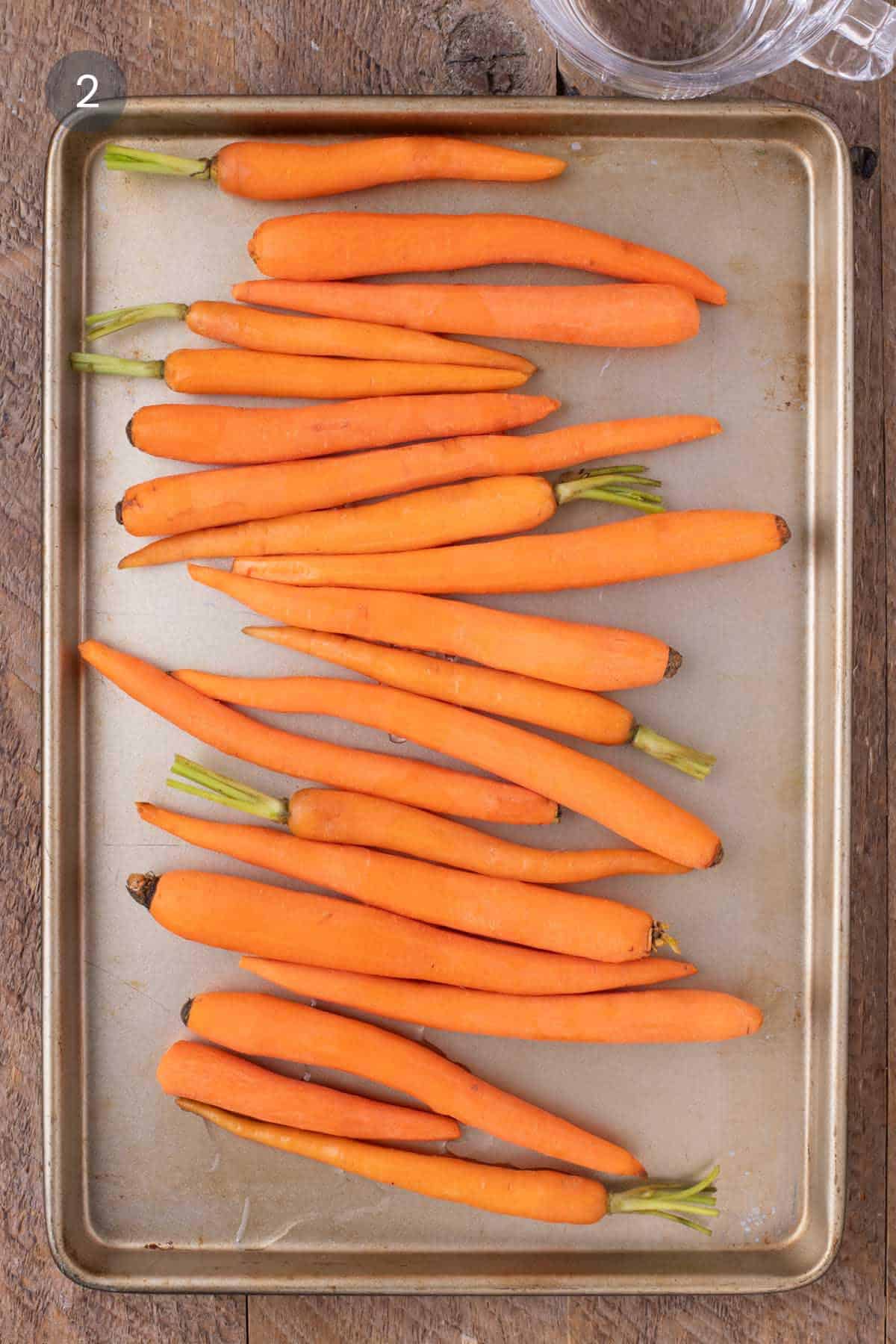Whole baby carrots arranged on a sheet pan before roasting