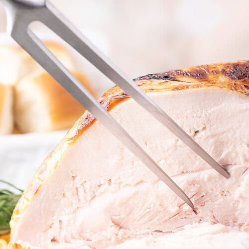 Close-up of sliced buttermilk brined turkey breast with golden, crispy skin on a platter with herbs.