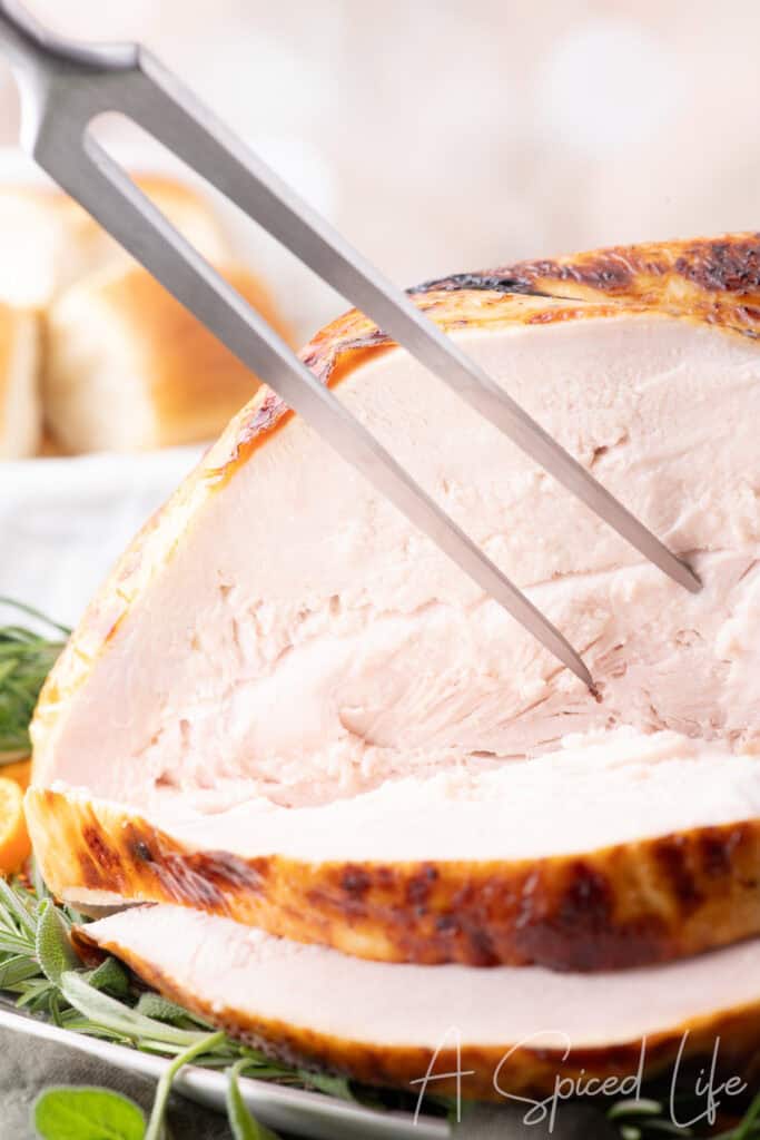 Close-up of sliced buttermilk brined turkey breast with golden, crispy skin on a platter with herbs.