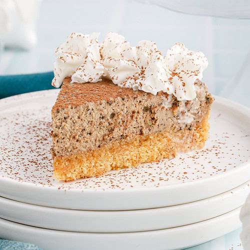 Slice of creamy coffee cheesecake topped with whipped cream and cocoa dusting on stacked white plates.