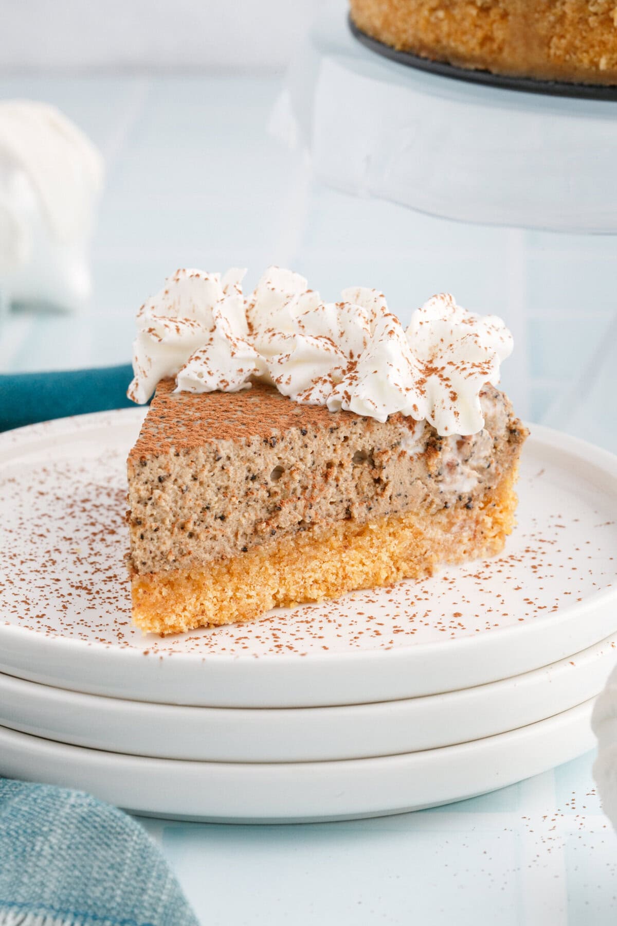 Slice of creamy coffee cheesecake topped with whipped cream and cocoa dusting on stacked white plates.