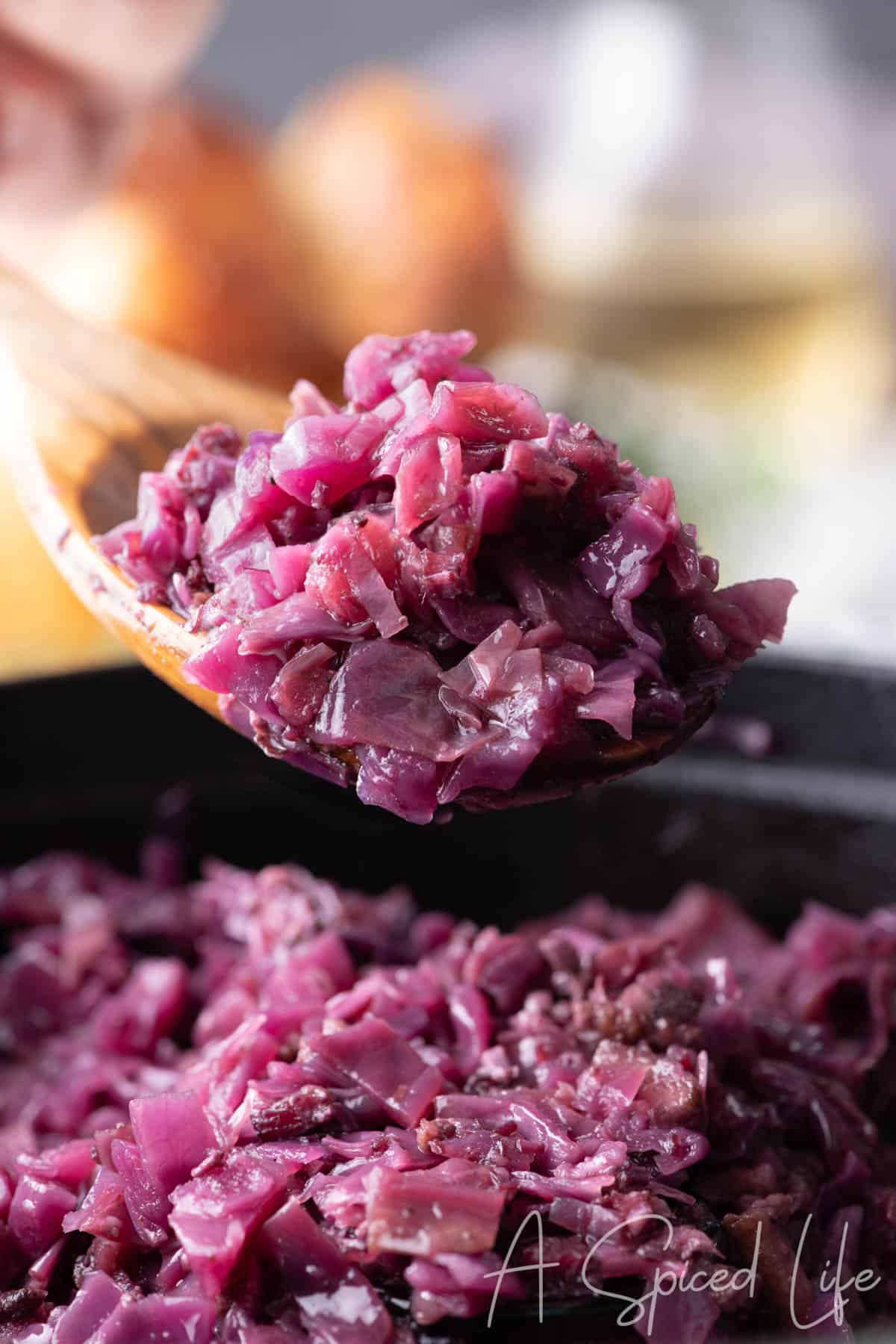 Spoonful of braised red cabbage over pot with blurred holiday background