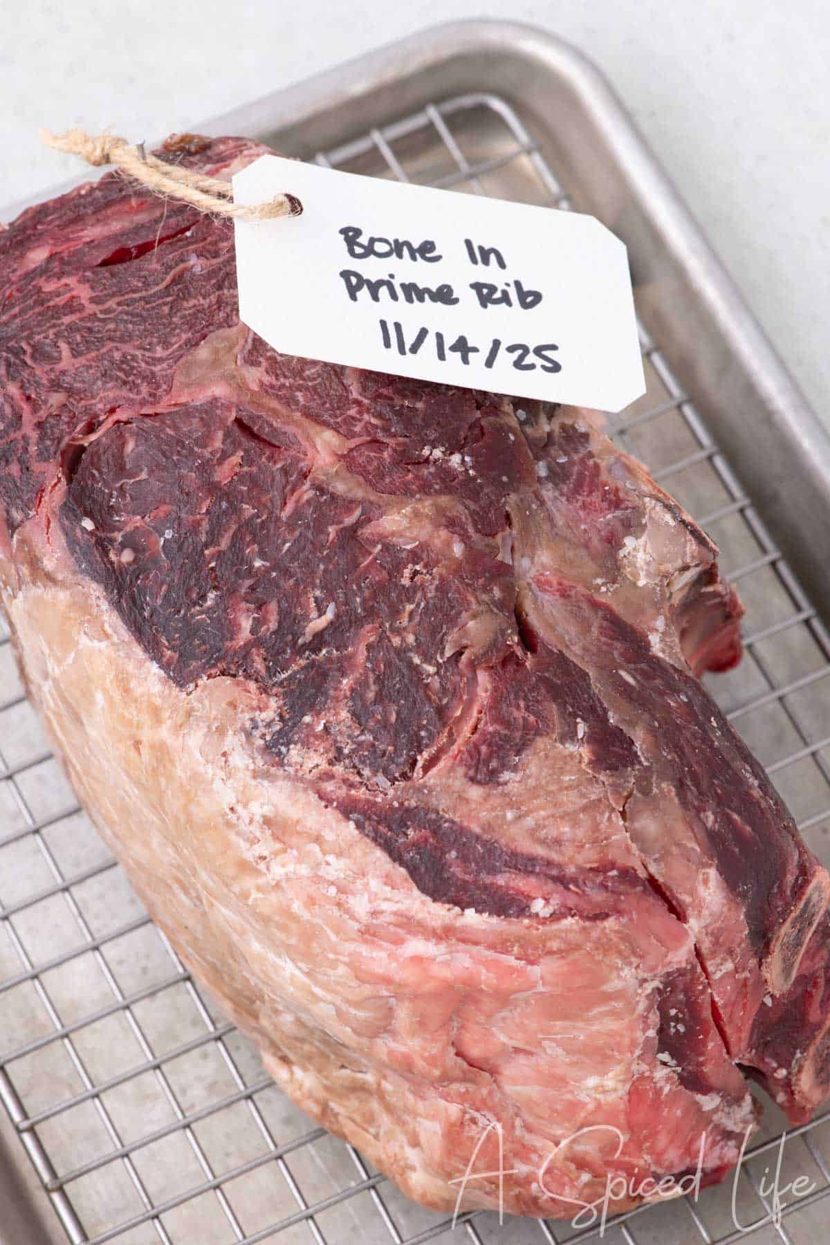 Five-day dry age beef at home with a labeled tag resting on a wire rack.