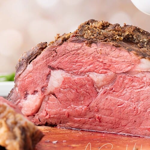 Medium-rare Dutch Oven Prime Rib being sliced on a wooden cutting board.