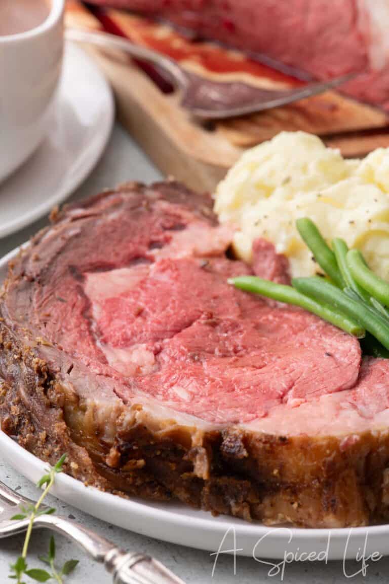 Sliced prime rib served with mashed potatoes and green beans on a white plate.