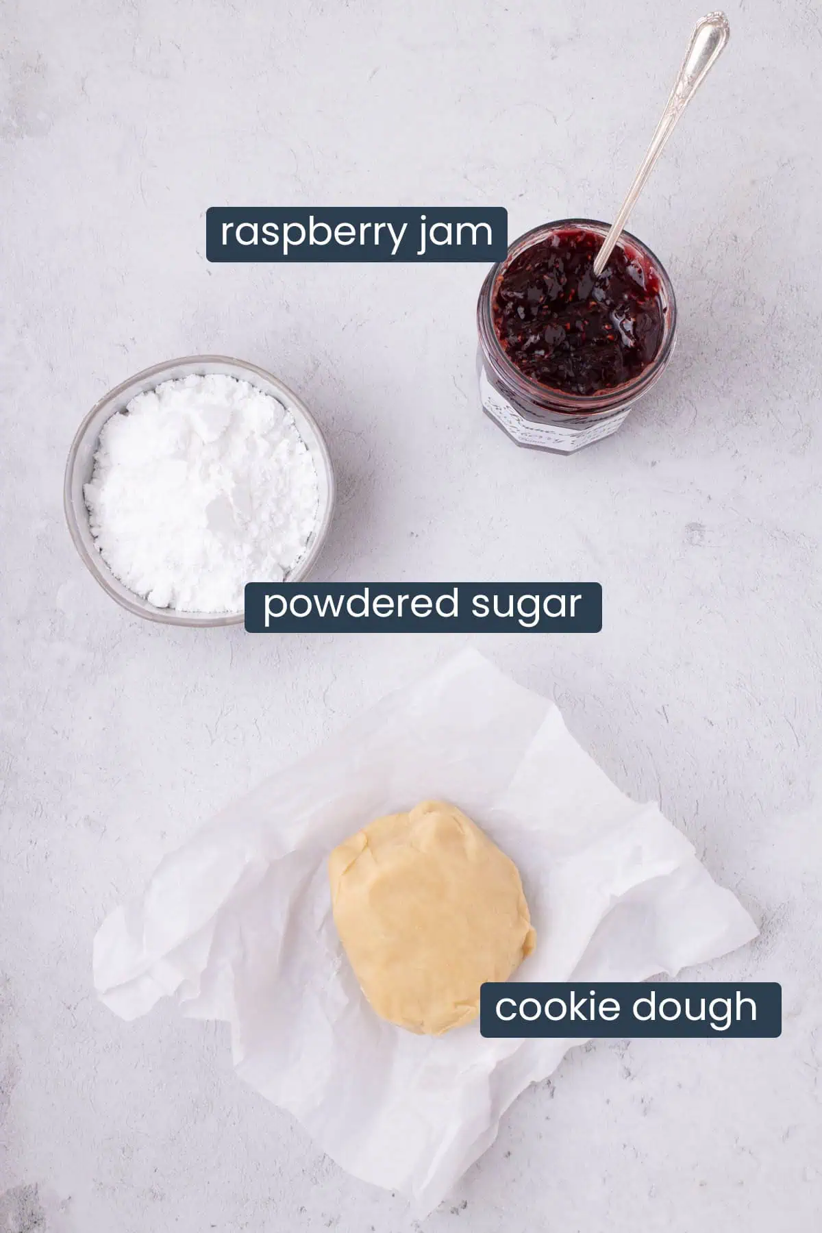 Ingredients for raspberry jam sandwich cookies, including cookie dough, powdered sugar, and raspberry jam, on a light surface./