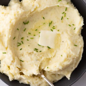 Creamy mashed potatoes topped with butter and chives in a serving bowl
