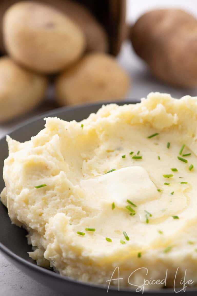 Creamy mashed potatoes with cheese served in a shallow bowl and topped with butter and chives