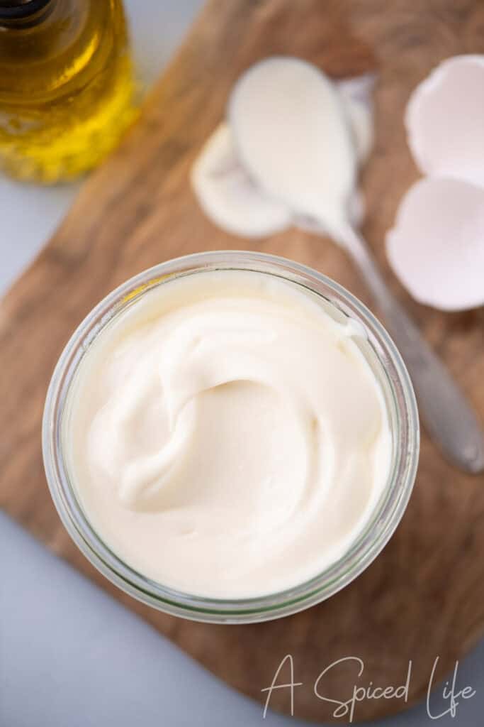 Top-down view of thick homemade mayonnaise in a small glass jar on a wooden board