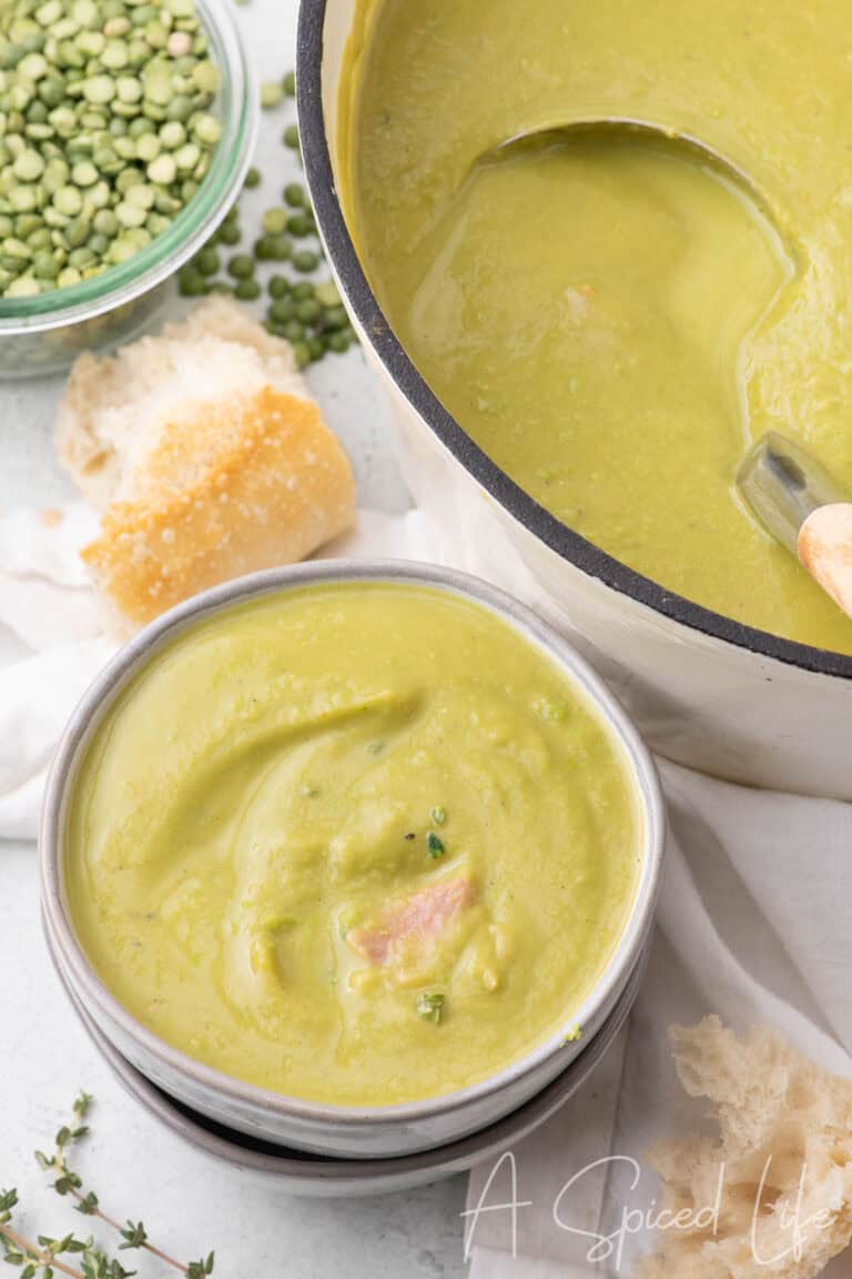 Bowl of creamy split pea soup with ham, shown alongside a pot of soup and pieces of crusty bread.