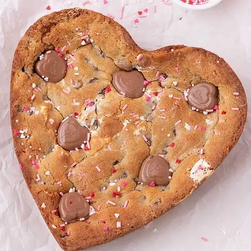 Chocolate chip cookie cake baked in a heart shaped pan with chocolate hearts and pink sprinkles