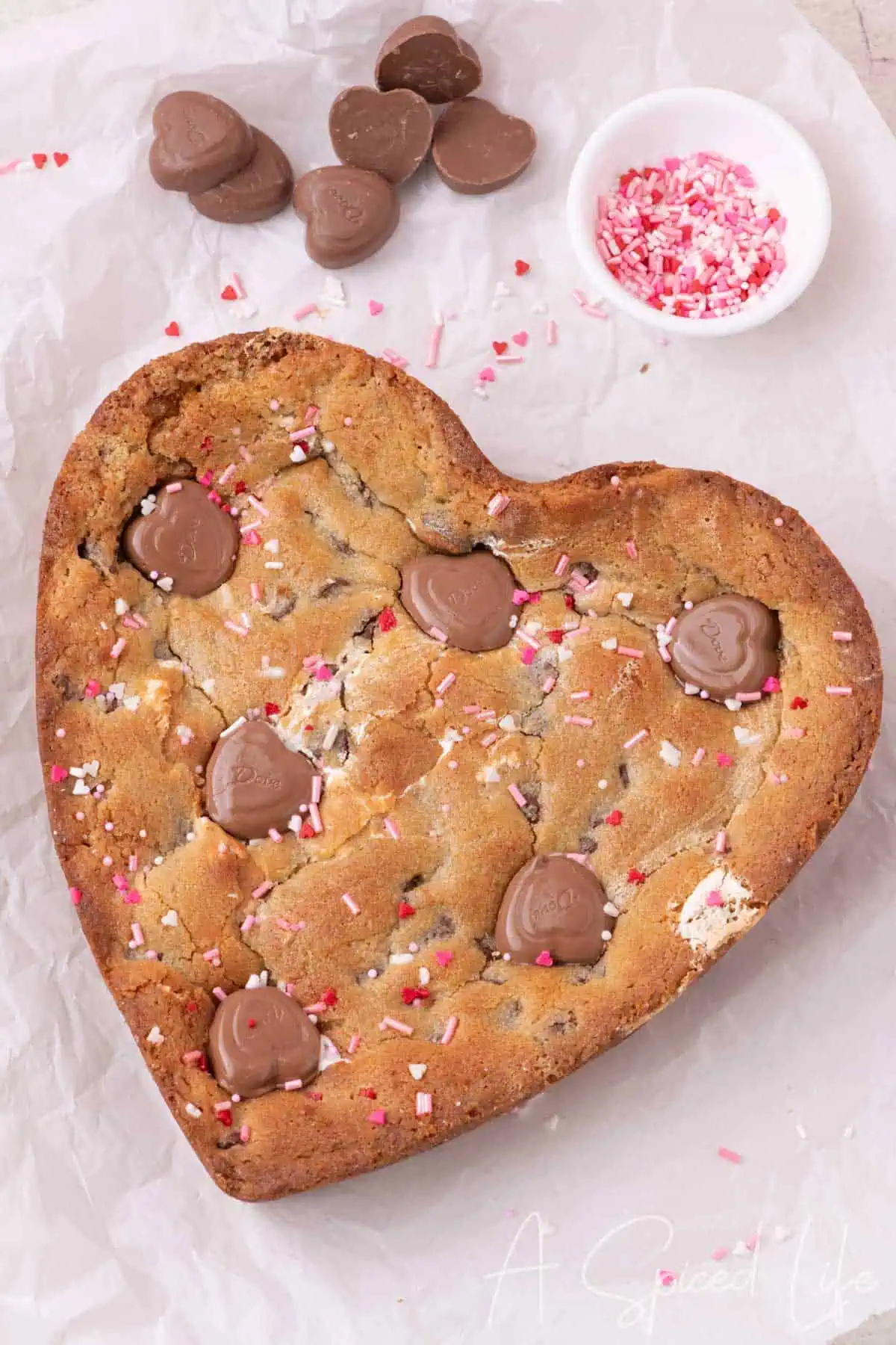 Chocolate chip cookie cake baked in a heart shaped pan with chocolate hearts and pink sprinkles