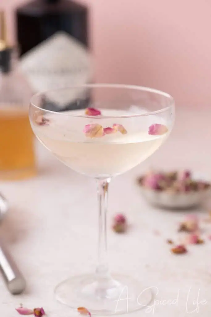 Close-up of a pale floral gin cocktail with rose petals floating on the surface