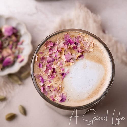 Two glasses of cardamom latte topped with crushed rose petals and light milk foam.