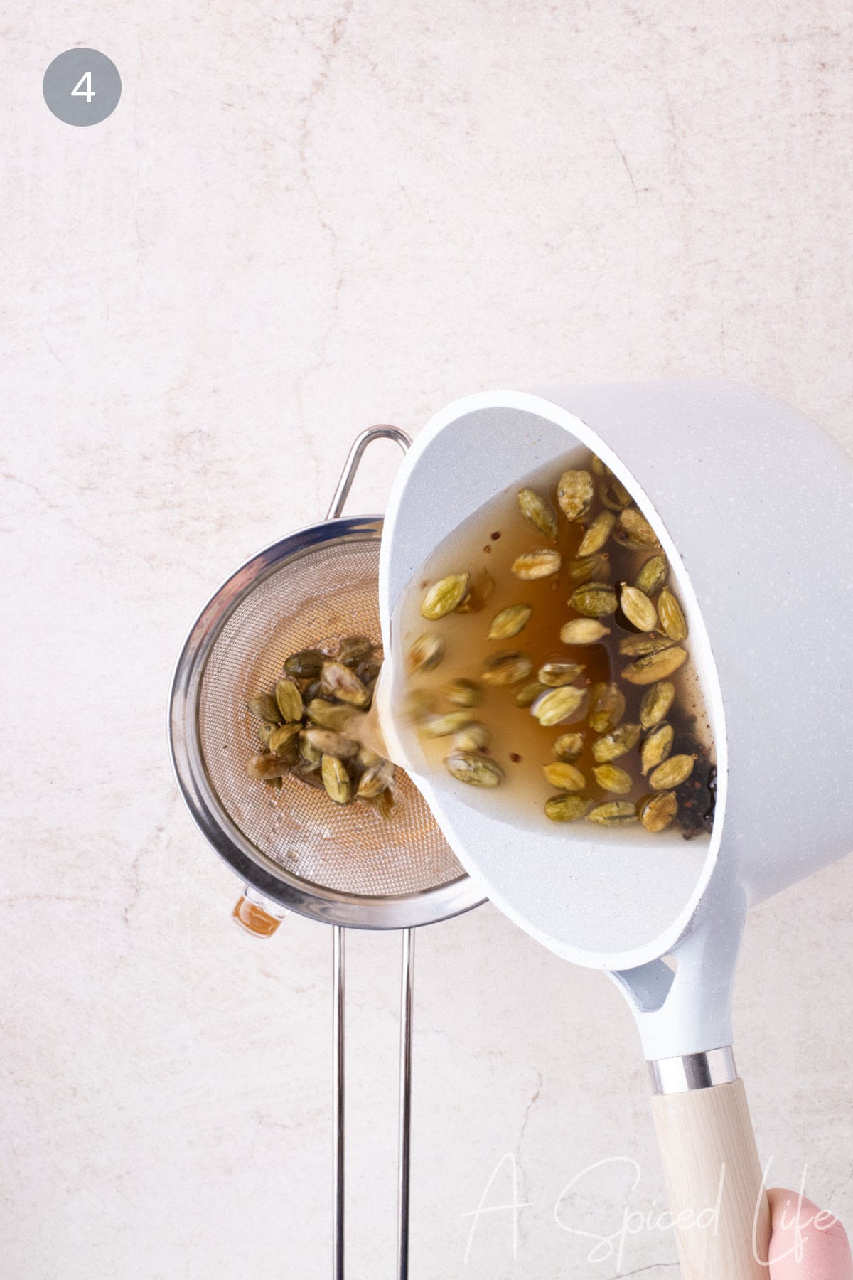 Straining hot cardamom syrup through a fine mesh sieve