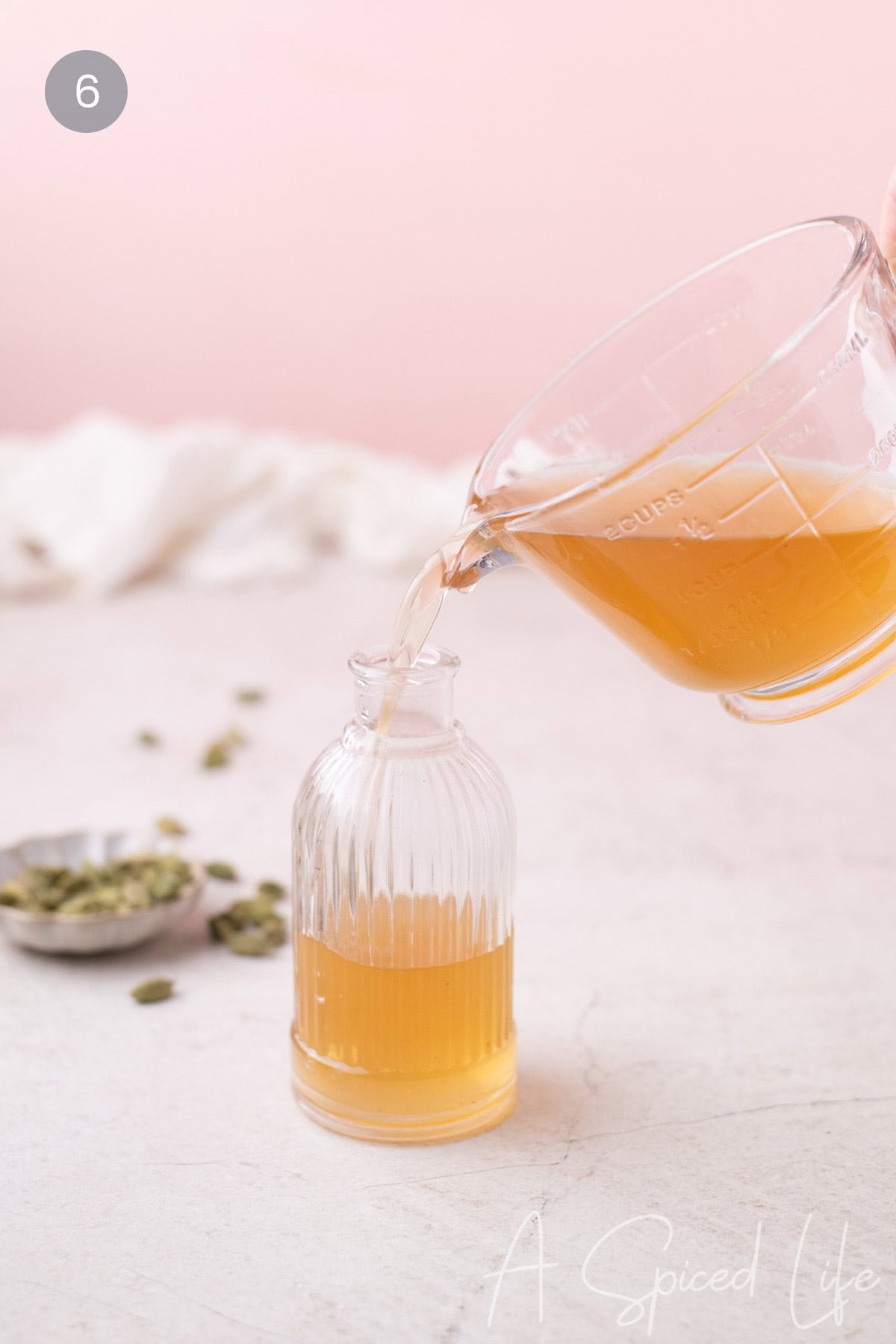 Pouring homemade rose cardamom simple syrup into a small glass bottle